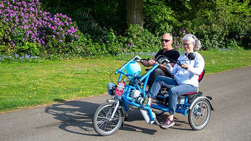 Two people riding a tandem bike in a nature setting