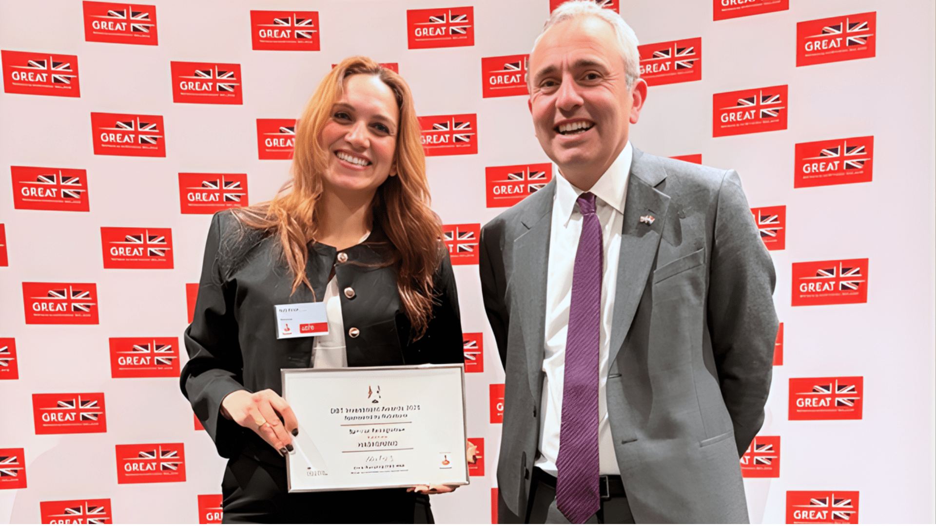 Two people standing in front of a backdrop featuring UK GREAT branding, with one person holding a certificate awarded to Haskoning at the DBT Investment Awards 2025.