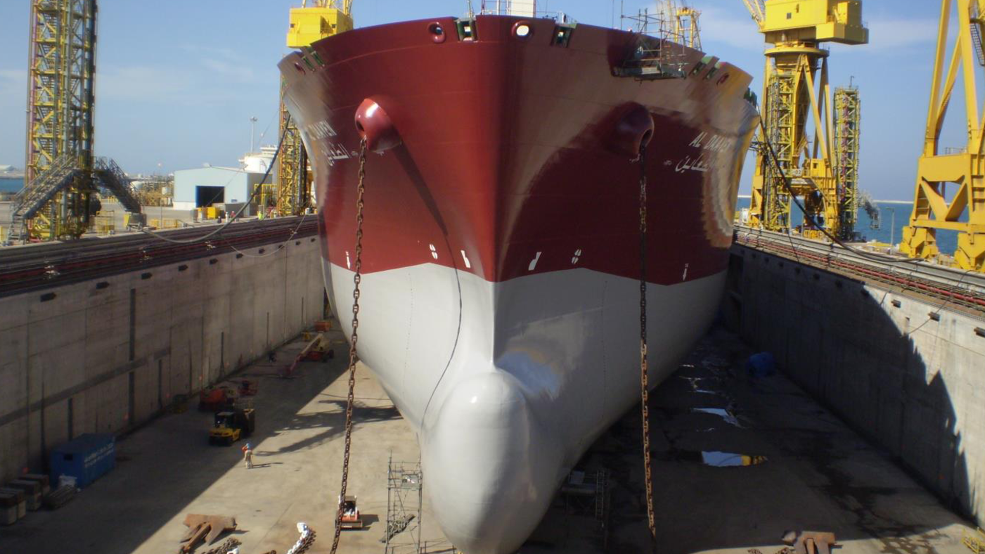 A large red tanker is being repaired in a dry dock at a shipyard.