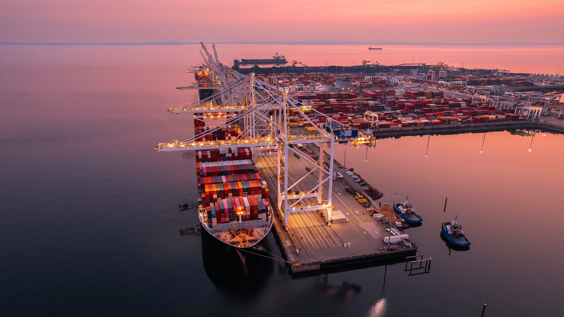 An aerial view of the Port of Vancouver container terminal in Canada at sunset, where shipping cargo is being loaded onto a container ship.