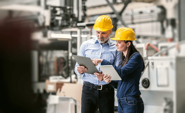 Industrial engineers wearing safety helmets reviewing process and plant design documents on a manufacturing site, discussing engineering details for industrial projects.