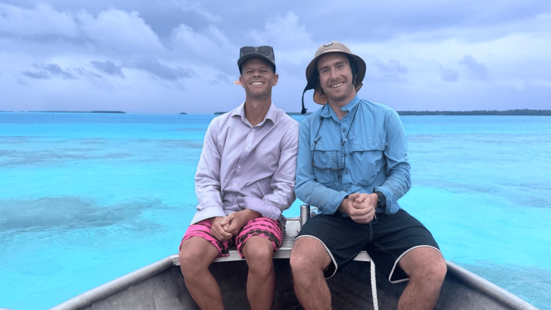 Josh Bluntschli sitting on the bow of a small boat in a turquoise lagoon beneath a cloudy sky.