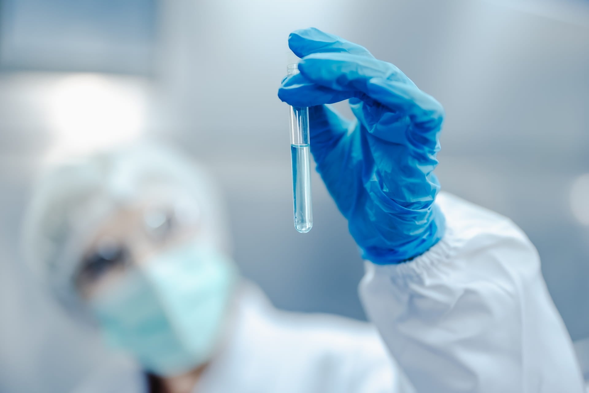 Scientist in protective clothing and blue gloves holding a test tube with a clear liquid