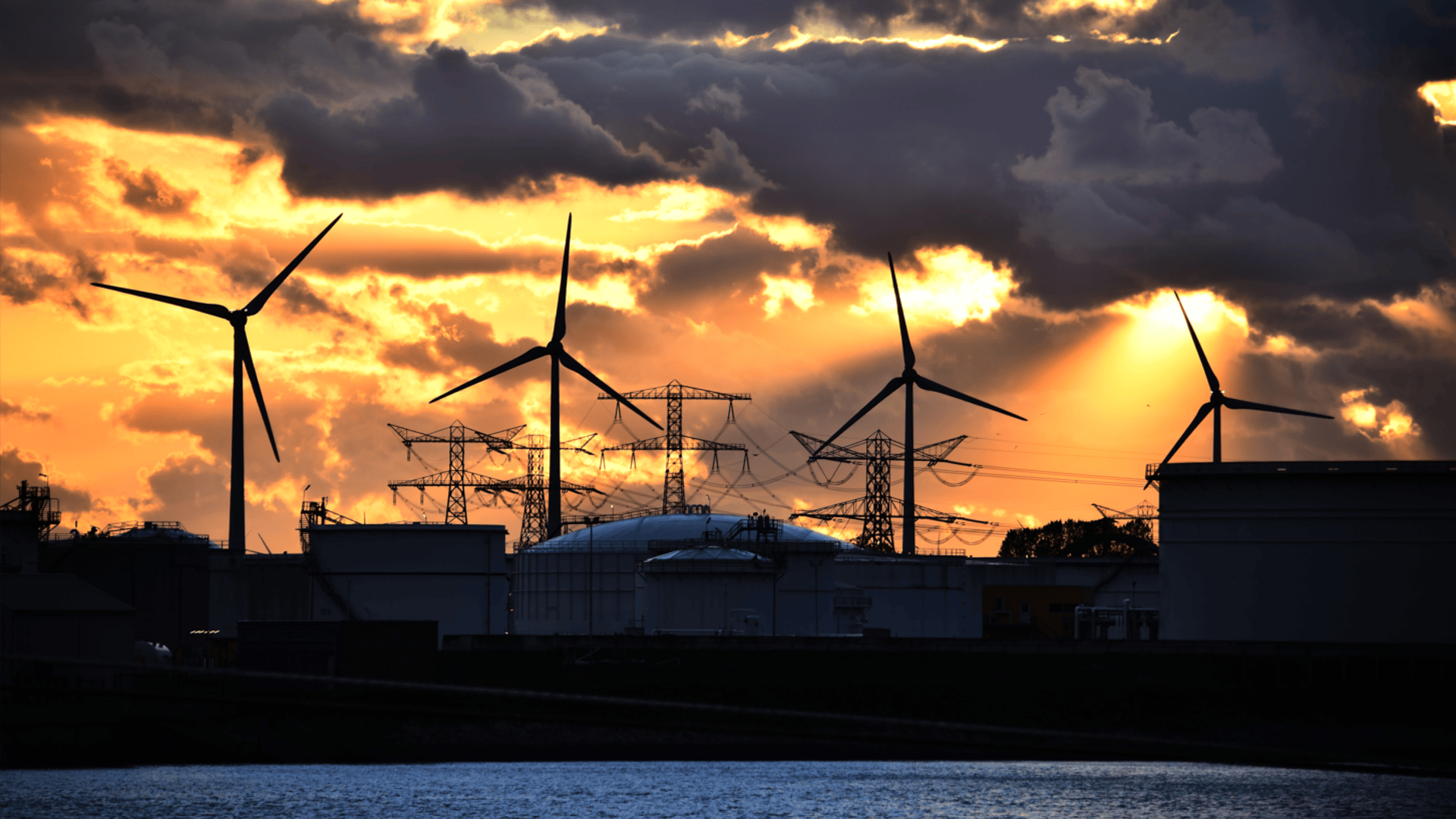 Wind turbines and industrial port infrastructure at sunset, representing port decarbonisation.