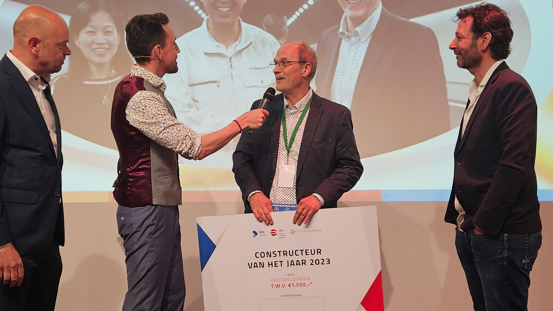 Hans de Wit awarded design engineer of the year during the award show. Hans is visible on the screen, with other people present at the location.