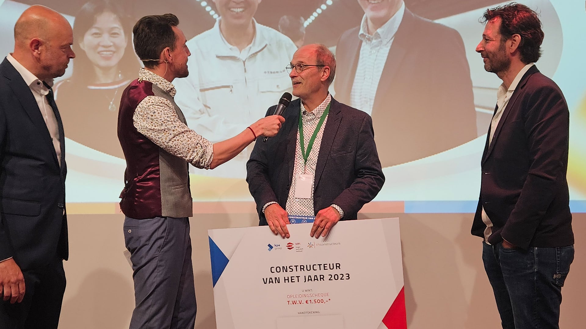 Hans de Wit awarded design engineer of the year during the award show. Hans is visible on the screen, with other people present at the location.