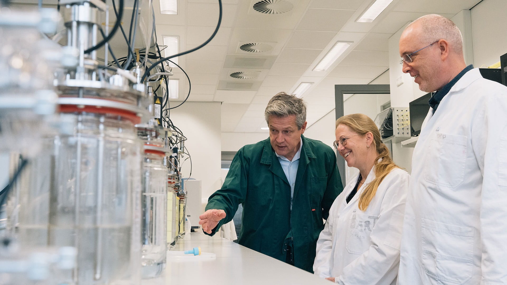 Three people looking at glass bottles in a laboratory