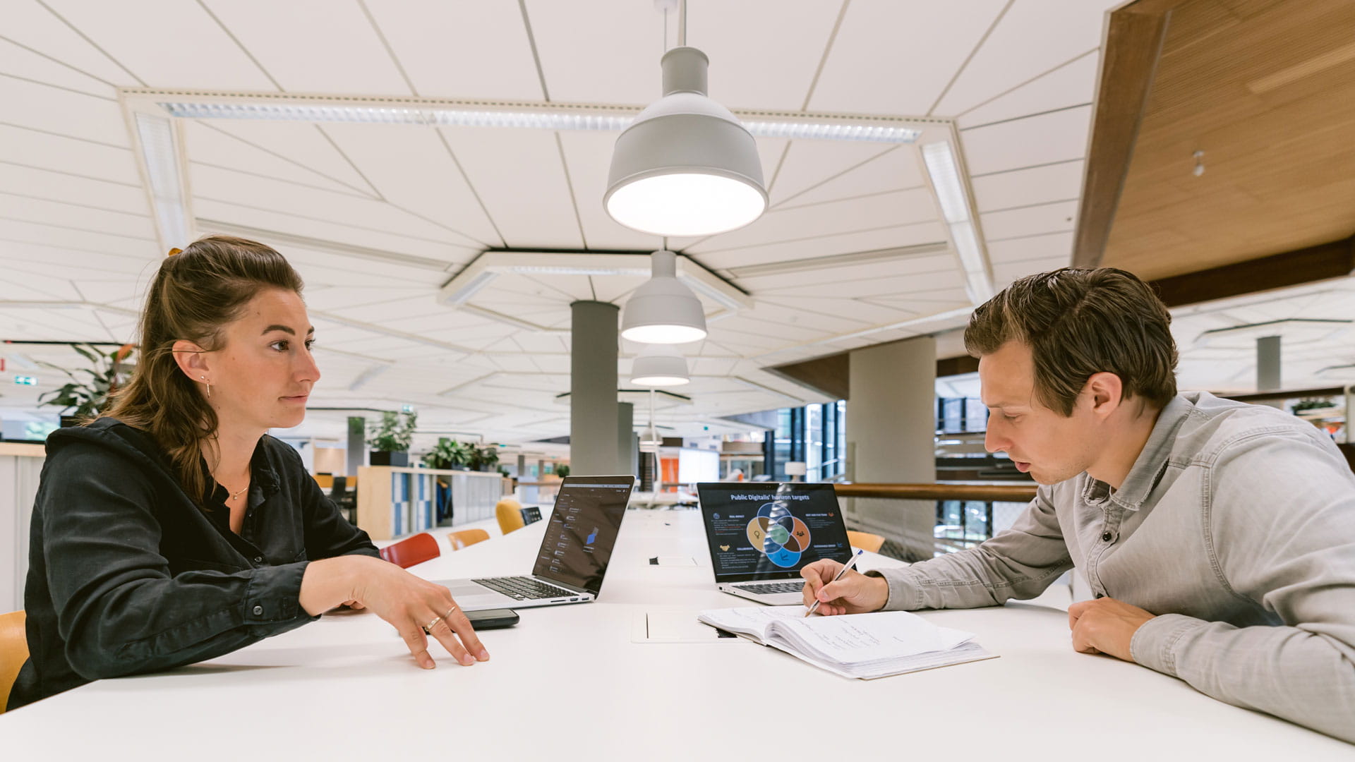 Two colleagues at a desk office discussing and taking notes