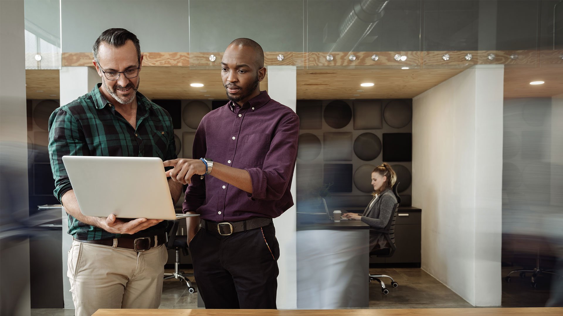 Two men analysing data on a laptop inside a building, discussing supply chain solutions and strategy consulting to achieve operational efficiency improvement