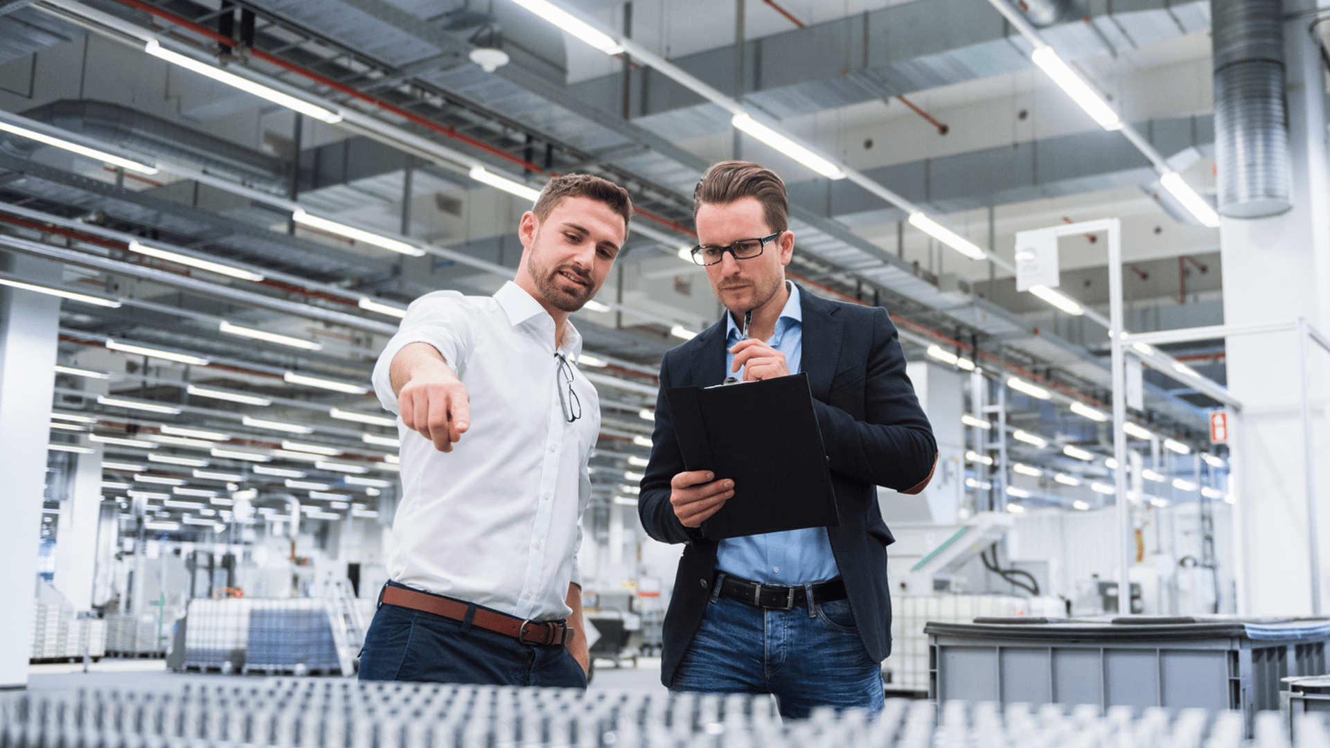 Two men in a manufacturing factory looking at a product belt discussing how to optimise their operations with industrial engineering and manufacturing services.