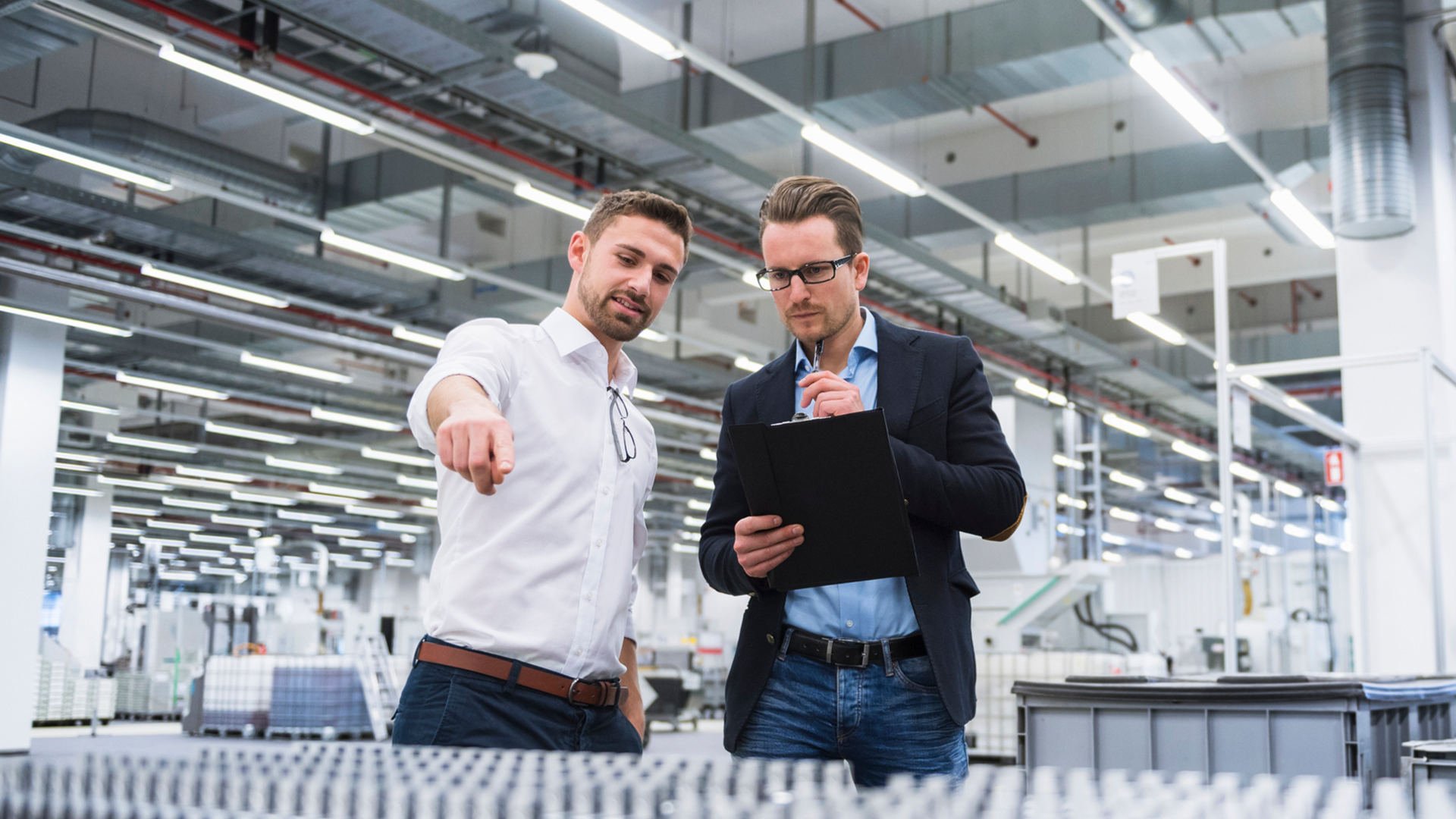 Two men in a manufacturing factory looking at a product belt discussing how to optimise their operations with industrial engineering and manufacturing services.