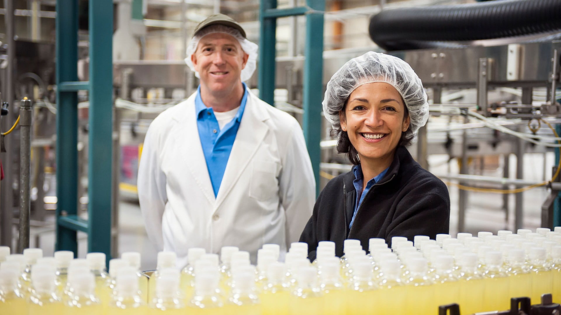 Factory workers inspecting production near an assembly line with bottled liquid.