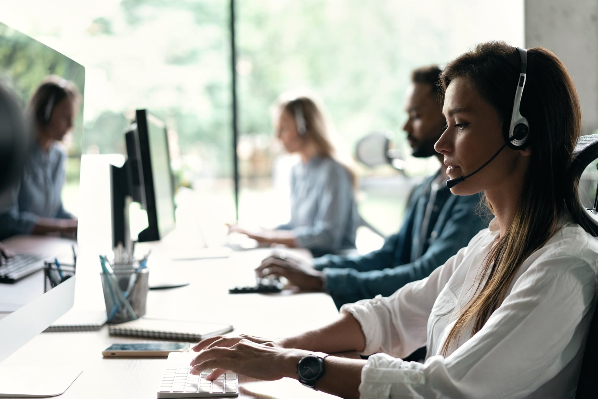 People working at a center, sitting at a computer and wearing headsets
